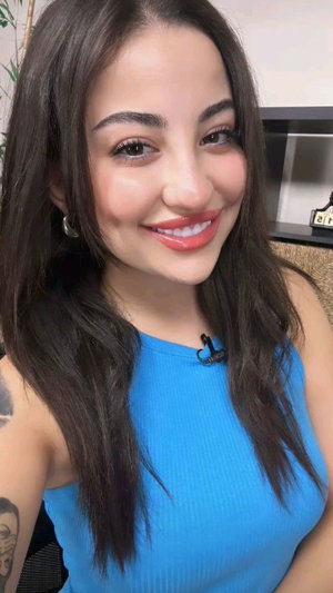 Woman with long dark hair in blue top, smiling, indoor setting.