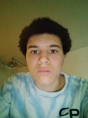 Young man with curly hair in tie-dye shirt indoors.
