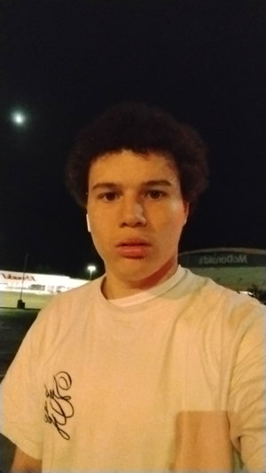 Man with curly hair wearing white t-shirt outdoors at night.