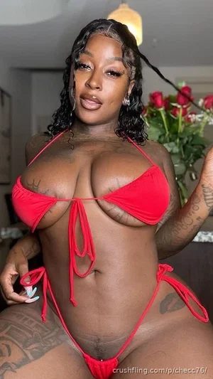 Woman in red bikini with tattoos, posing indoors near roses.
