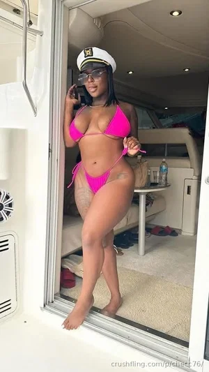 Woman in pink bikini and captain hat standing in yacht doorway, holding sunglasses.
