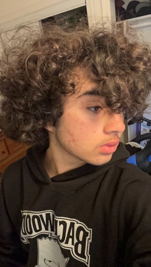 Young man with curly hair wearing black hoodie indoors.