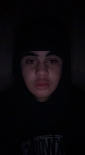 Man in black hoodie taking a selfie in dim lighting.