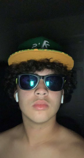 Shirtless man with curly hair wearing cap and sunglasses.