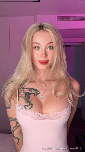 Blonde woman in pink lace camisole with snake tattoo, indoors under purple lighting.