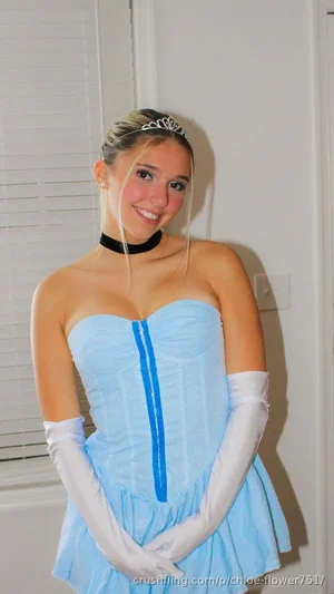Woman in light blue strapless dress with white gloves and tiara, smiling indoors.