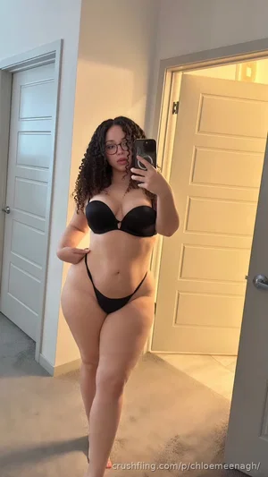 Woman with curly hair in black lingerie taking mirror selfie indoors.