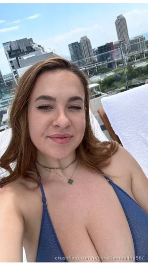 Woman in blue bikini top on rooftop with city skyline behind.
