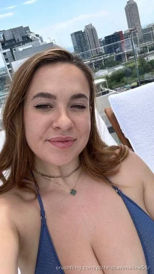 Woman in blue bikini top on rooftop with city skyline behind.