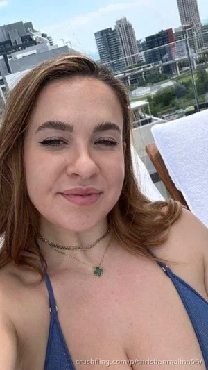 Woman in blue bikini top on rooftop with city view, wearing necklace.