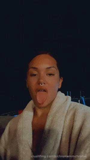 Woman in white robe, tongue out, dark background, indoor setting.