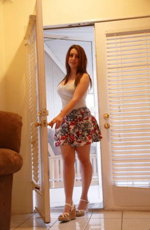 Woman in white top and floral skirt standing in doorway.