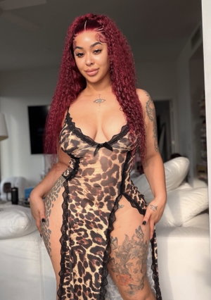 Woman with red curly hair in leopard print lingerie with black lace, standing in a bedroom.