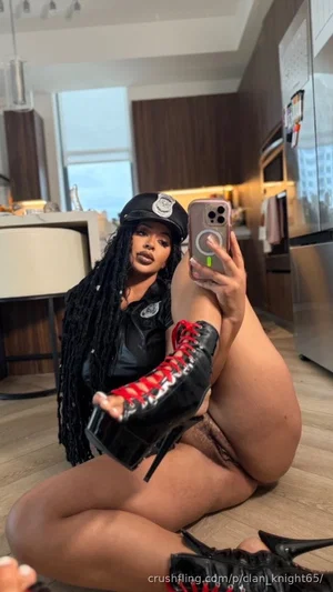 Woman in police-themed outfit and high boots posing on kitchen floor.