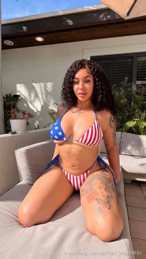 Woman in red white blue bikini with tattoos posing on outdoor sofa.