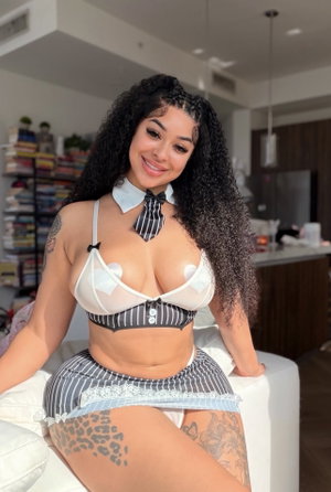 Curvy woman with curly hair in sheer lingerie and striped skirt indoors.