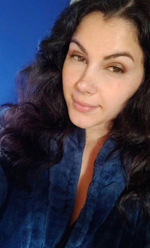 Woman with dark curly hair in a blue robe, indoor selfie.