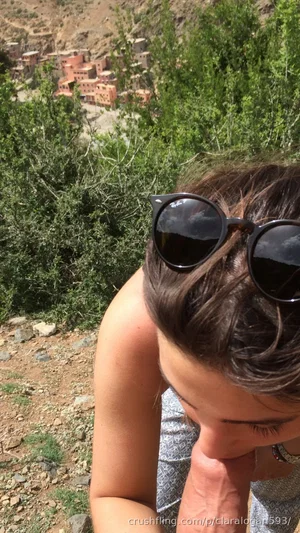 Woman with sunglasses on head, wearing tank top, outdoors in rocky hilly area with greenery and