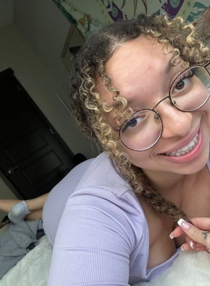 Smiling woman with curly blonde hair and glasses in purple top indoors.