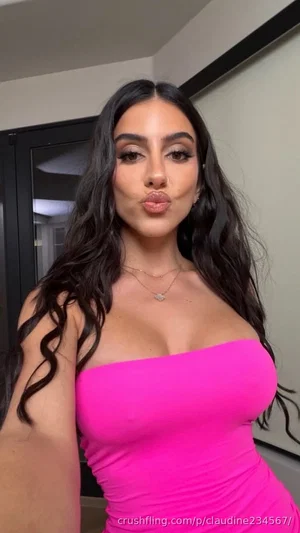 Woman with long dark hair in a bright pink strapless top, posing indoors.