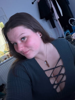Woman with brown hair in dark ribbed top with lace-up front, indoors.
