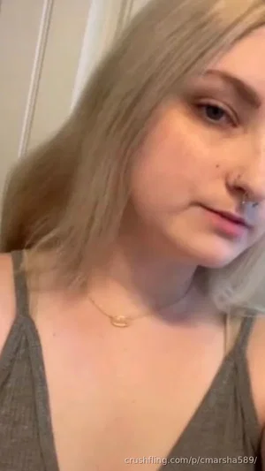 Blonde woman in a gray tank top, indoor selfie, neutral expression.