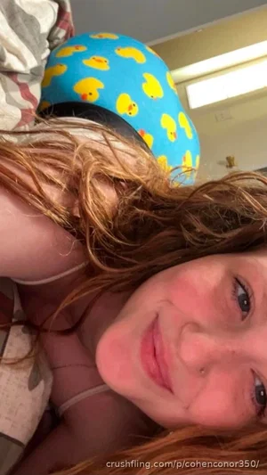 Woman with red hair wearing a blue duck-patterned hat, lying down indoors.