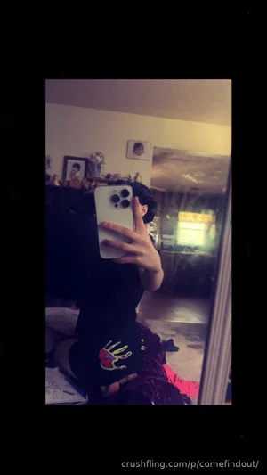 Woman in black top and shorts taking mirror selfie in bedroom.