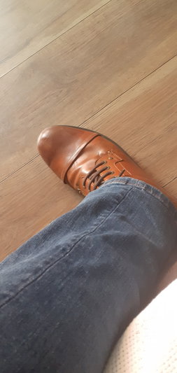 Foot in brown leather shoe and blue jeans on wood floor