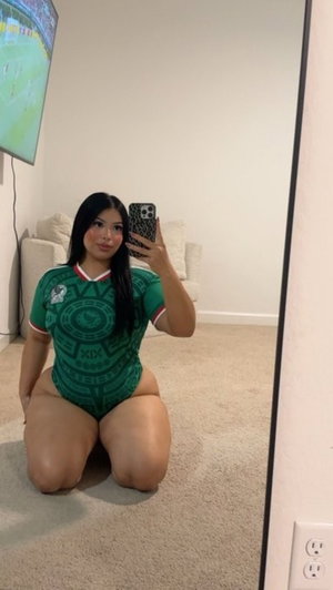 Woman in green sports jersey kneeling on carpet in front of mirror, indoor setting.
