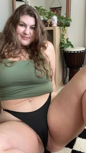 Woman with curly hair in green crop top and black underwear, sitting indoors.