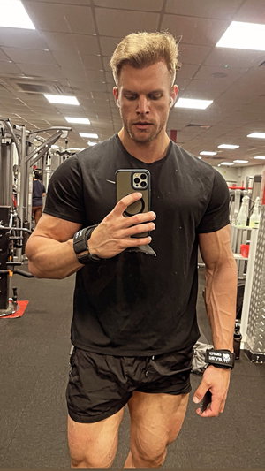 Muscular man in black t-shirt taking mirror selfie in gym.