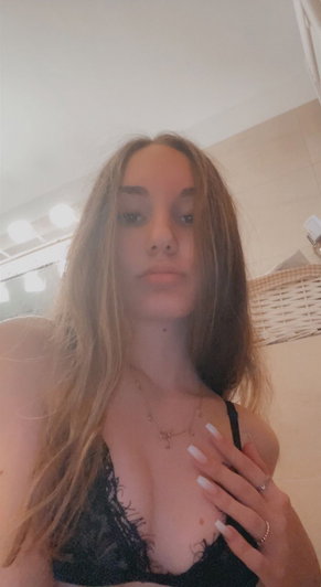 Woman with long brown hair in black lace bra taking selfie.