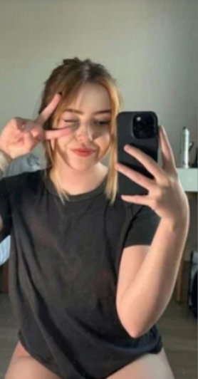 Woman in black t-shirt taking mirror selfie, showing legs, indoor setting.