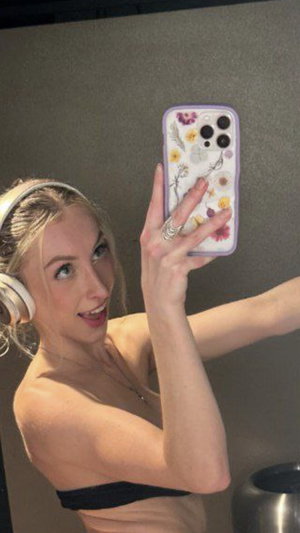 Blonde woman in black bandeau top taking mirror selfie with floral phone case.