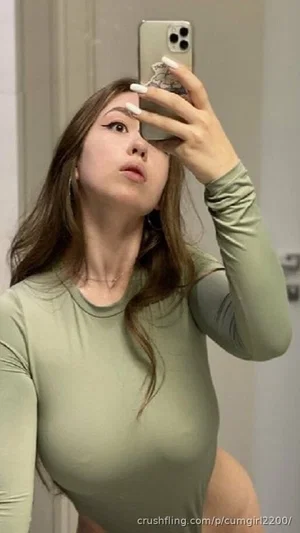 Woman in olive green long-sleeve top taking mirror selfie, indoor setting.