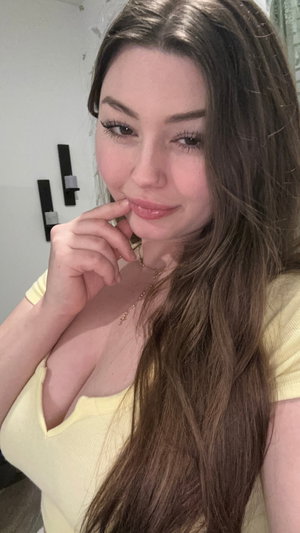 Brunette woman in yellow top taking close-up selfie indoors.