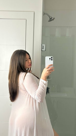 Brunette woman in sheer white dress taking bathroom mirror selfie