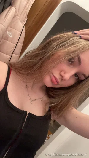 Woman with blonde hair in black top, posing indoors near wardrobe.