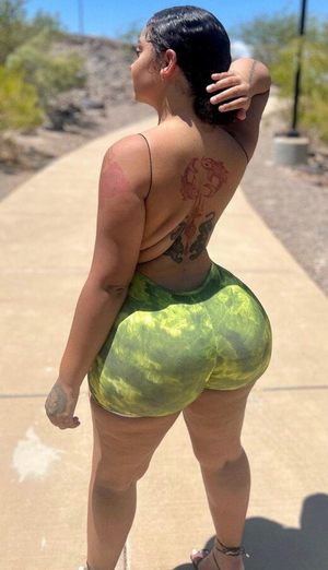 Woman in green patterned shorts and thin straps, standing outdoors on a path, back view with