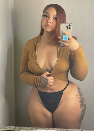 Curvy woman with red hair taking mirror selfie in brown top.
