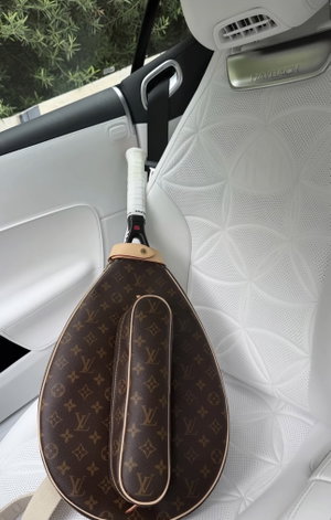 LV tennis bag on Maybach car seat with greenery outside.