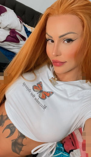 Woman with long orange hair in white crop top, showing tattooed side, indoors.