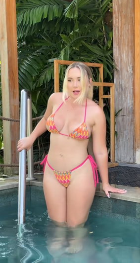 Woman in colorful bikini standing in pool, surrounded by tropical plants.