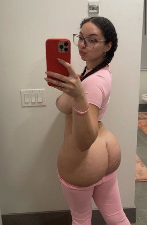 Woman in pink crop top and leggings takes mirror selfie in bathroom.