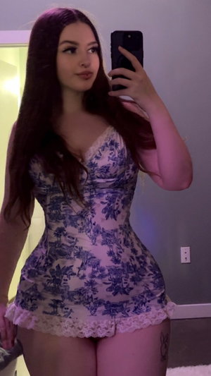 Woman with long dark hair taking mirror selfie in floral dress.