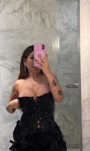 Woman in black sequined corset top and skirt in bathroom mirror selfie.