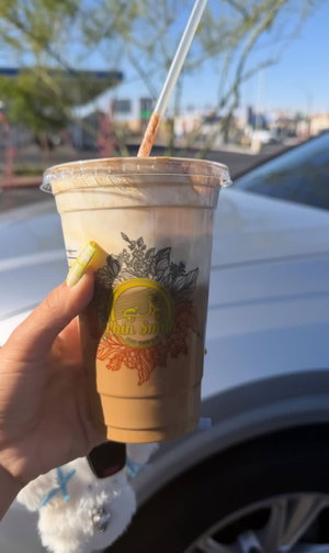 Hand holding iced coffee cup in car.