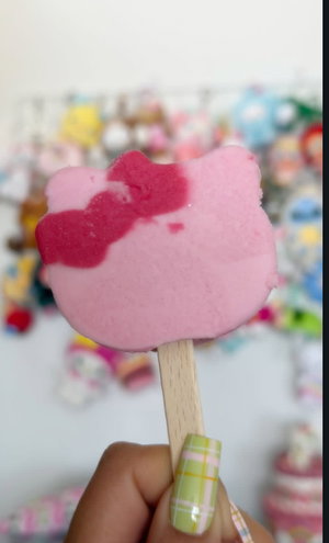 Hand holding pink Hello Kitty popsicle amid toys.