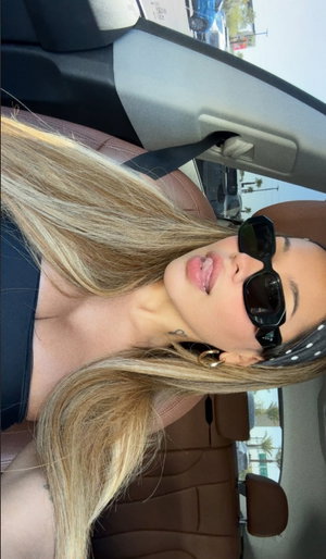Blonde woman in black top taking selfie in car.